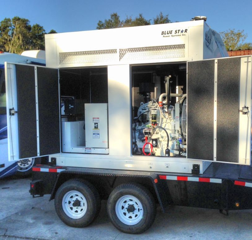 Open trailer-mounted industrial machine with open doors, hoses, and gauges, parked outdoors.