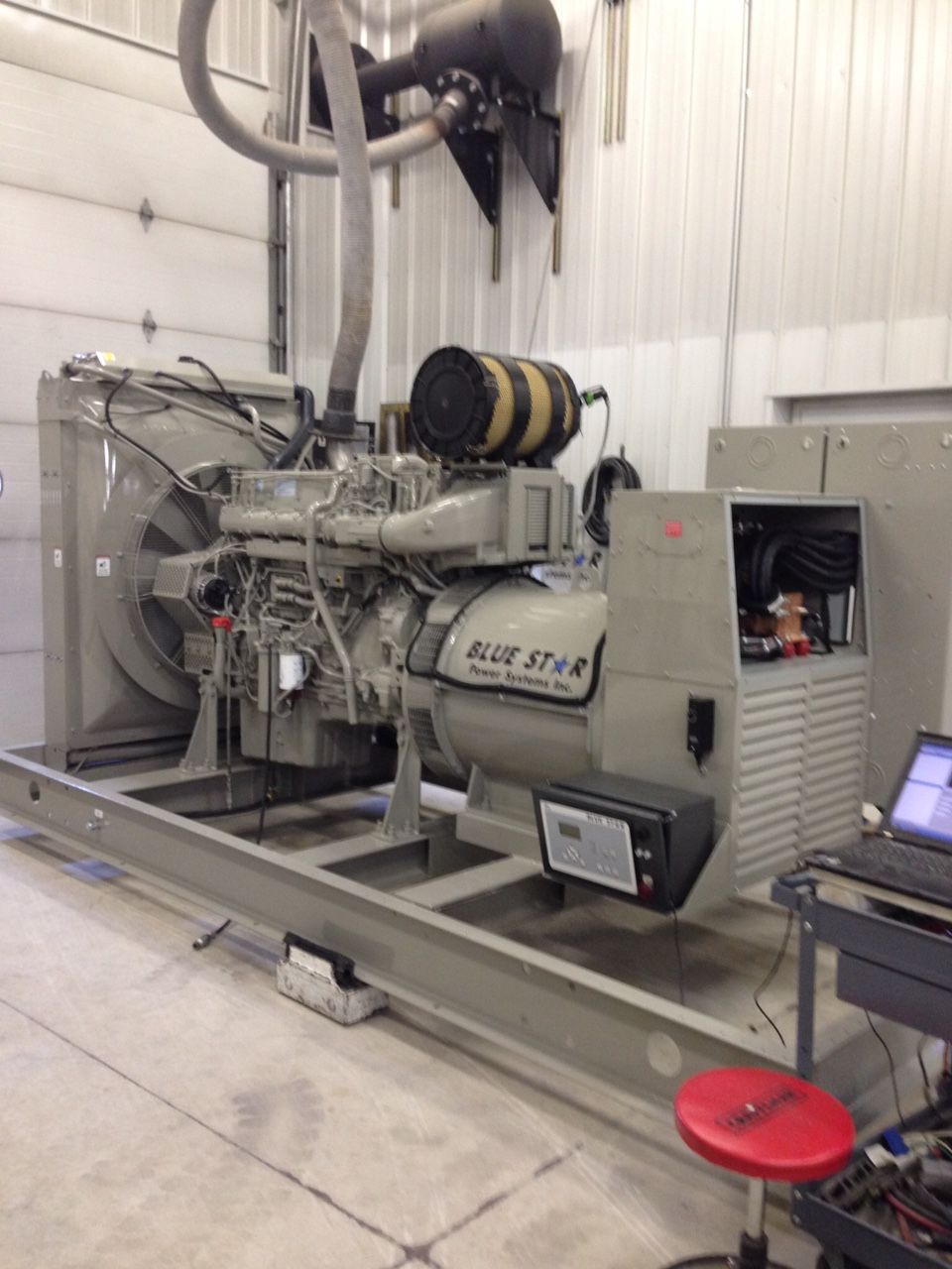 Large industrial generator set inside a white-walled room with a laptop on a small cart nearby