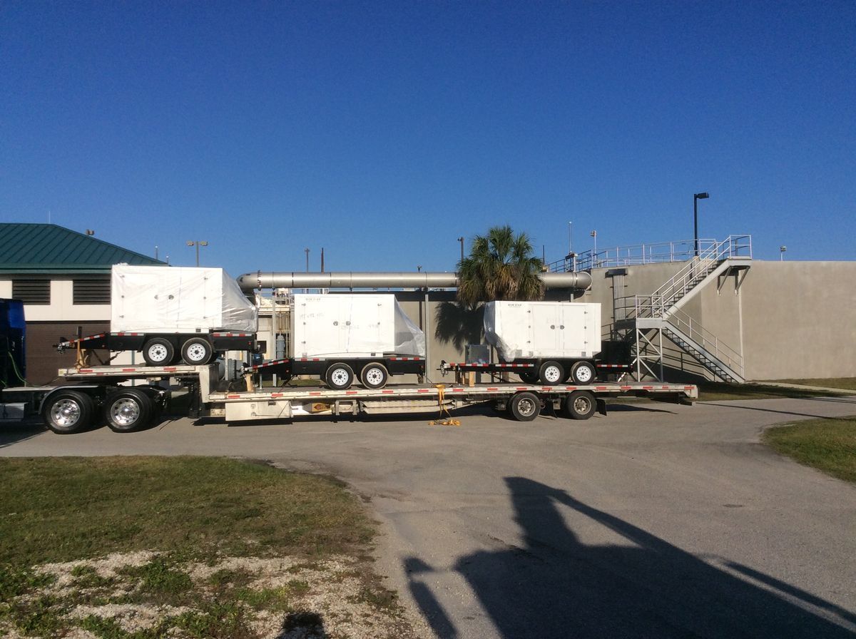 Three white trucks with trailers parked beside a building under a clear blue sky