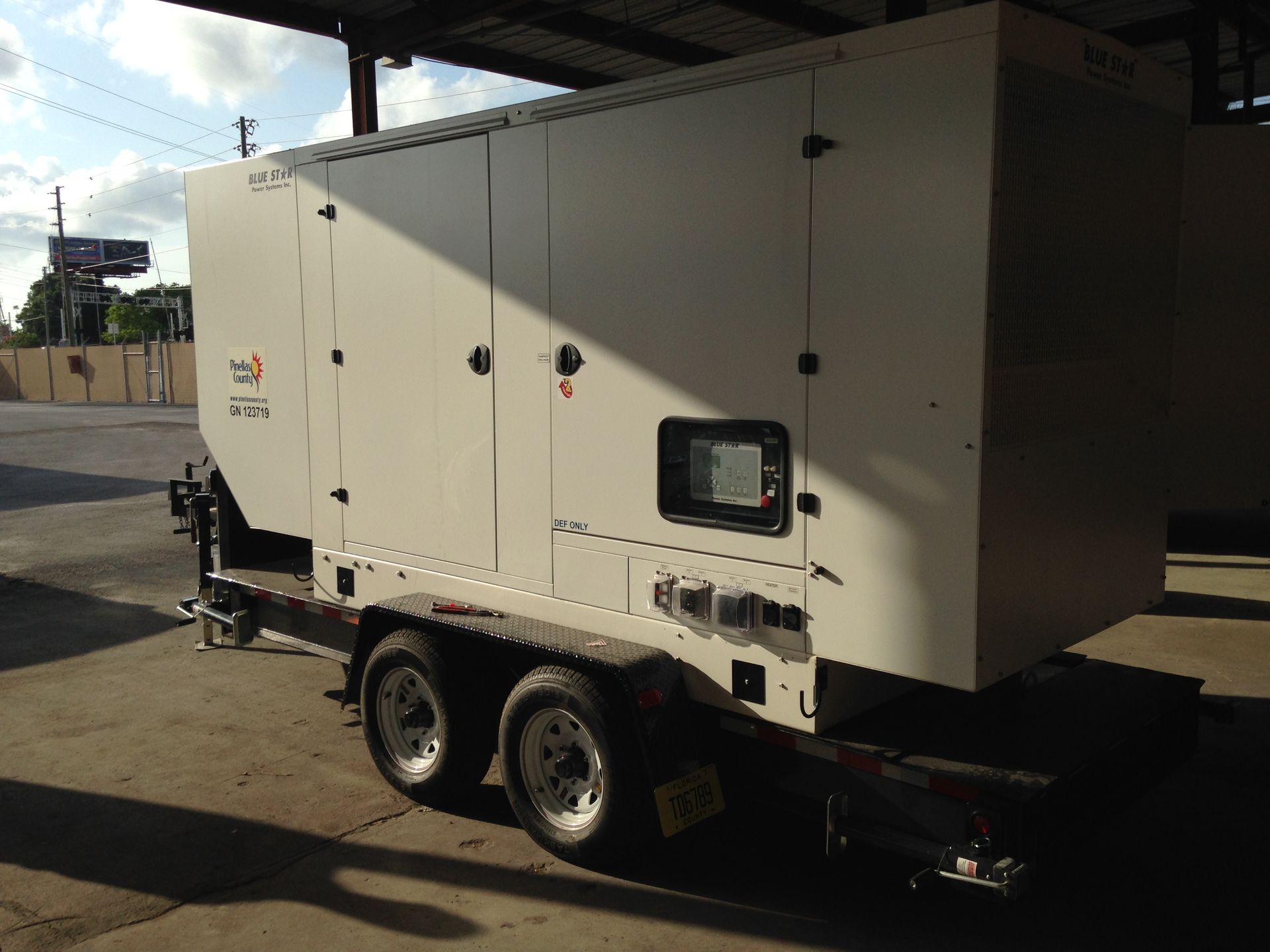 White dual-axle trailer-mounted generator parked outdoors in an industrial lot.