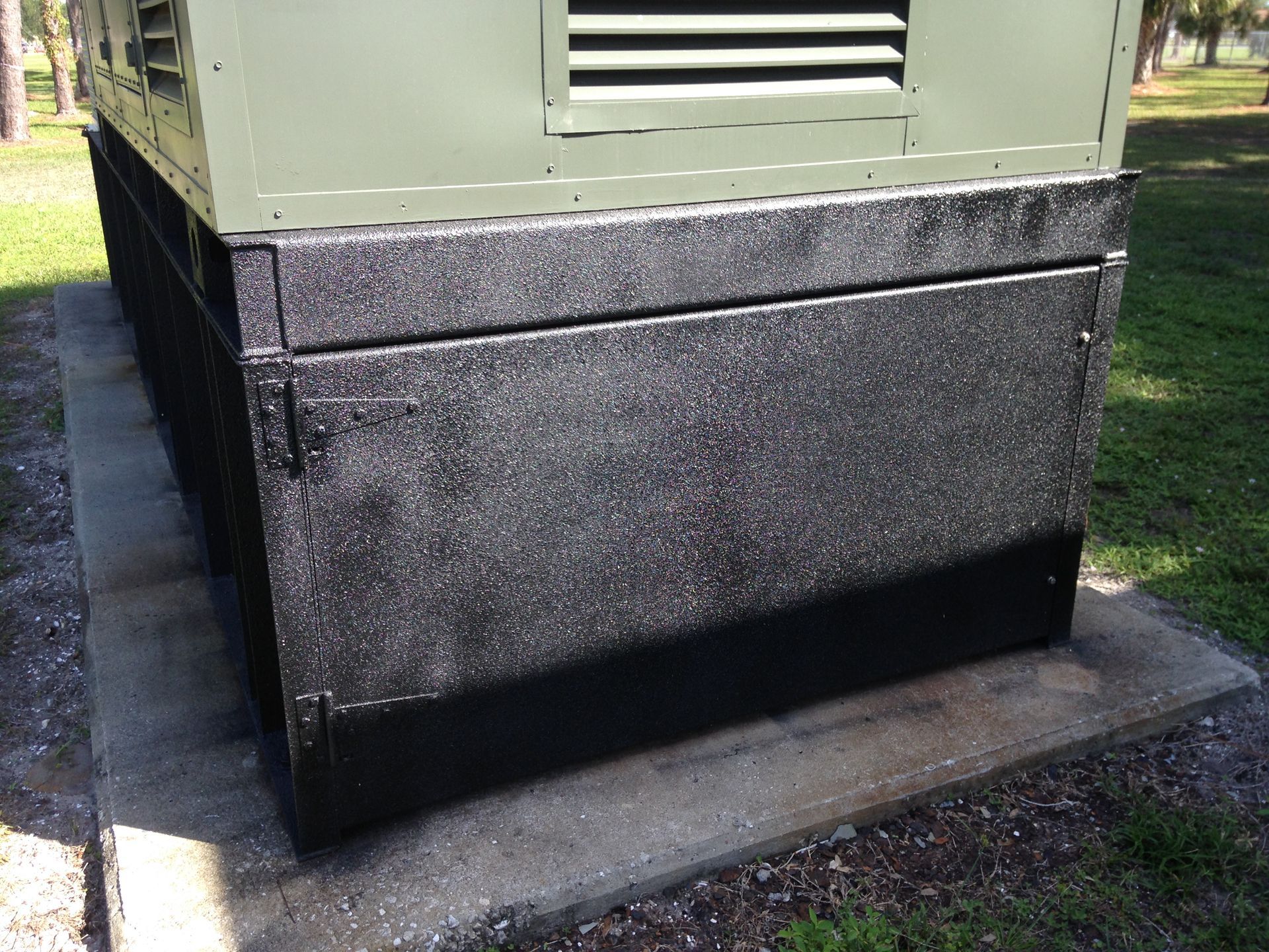 Green building base with black textured foundation trim beside a sidewalk and grass.