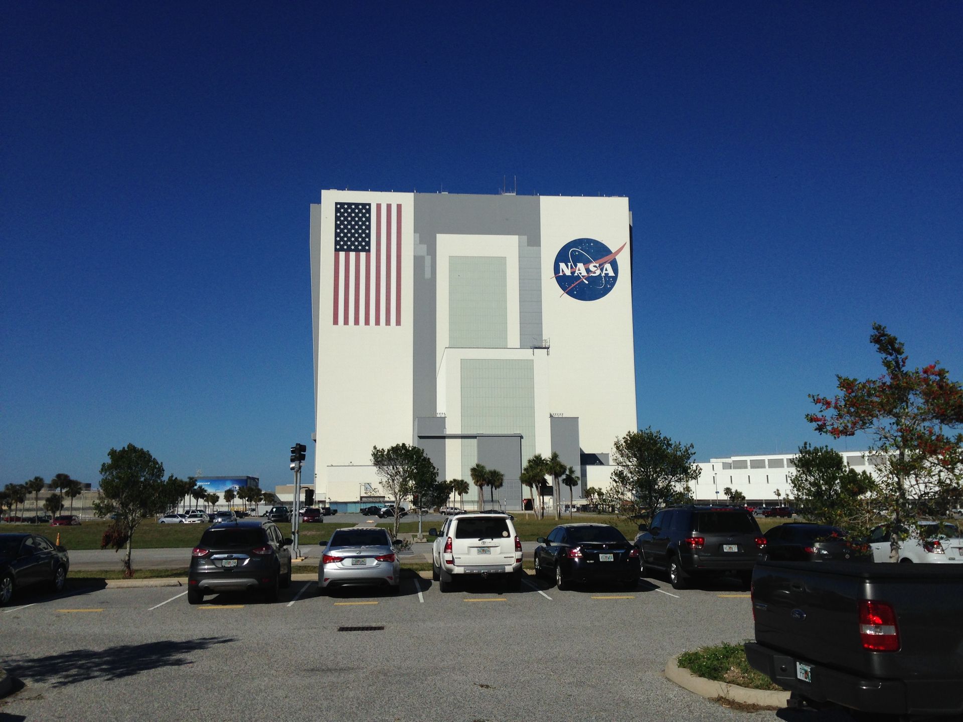 NASA building with American flag facade, parked cars in front, under a clear blue sky