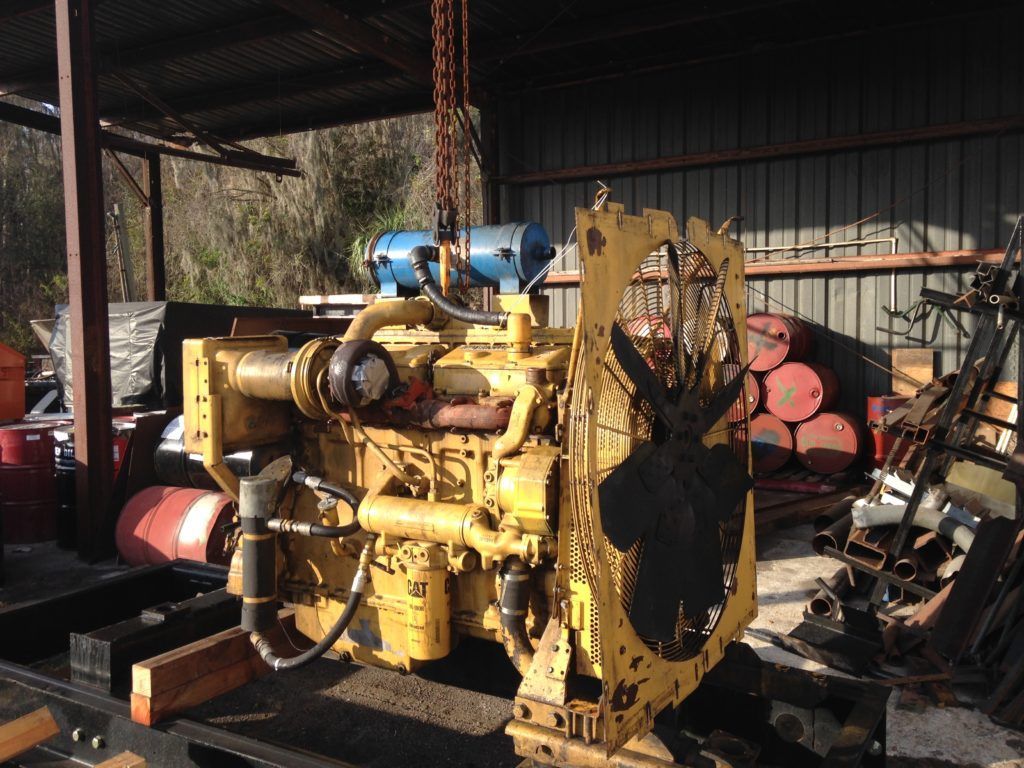 Yellow industrial machine in a shed, with pipes, hoses, and rusted metal parts scattered nearby.