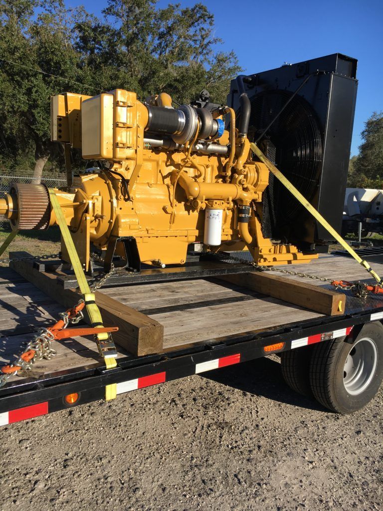 Yellow industrial generator on a flatbed trailer in a gravel lot, with a black cover behind it.