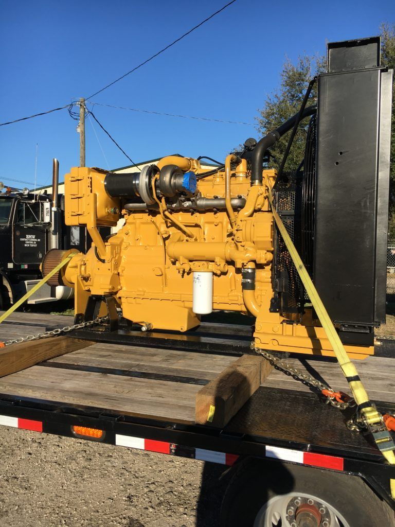 Yellow industrial generator secured on a flatbed trailer outdoors under a clear blue sky.