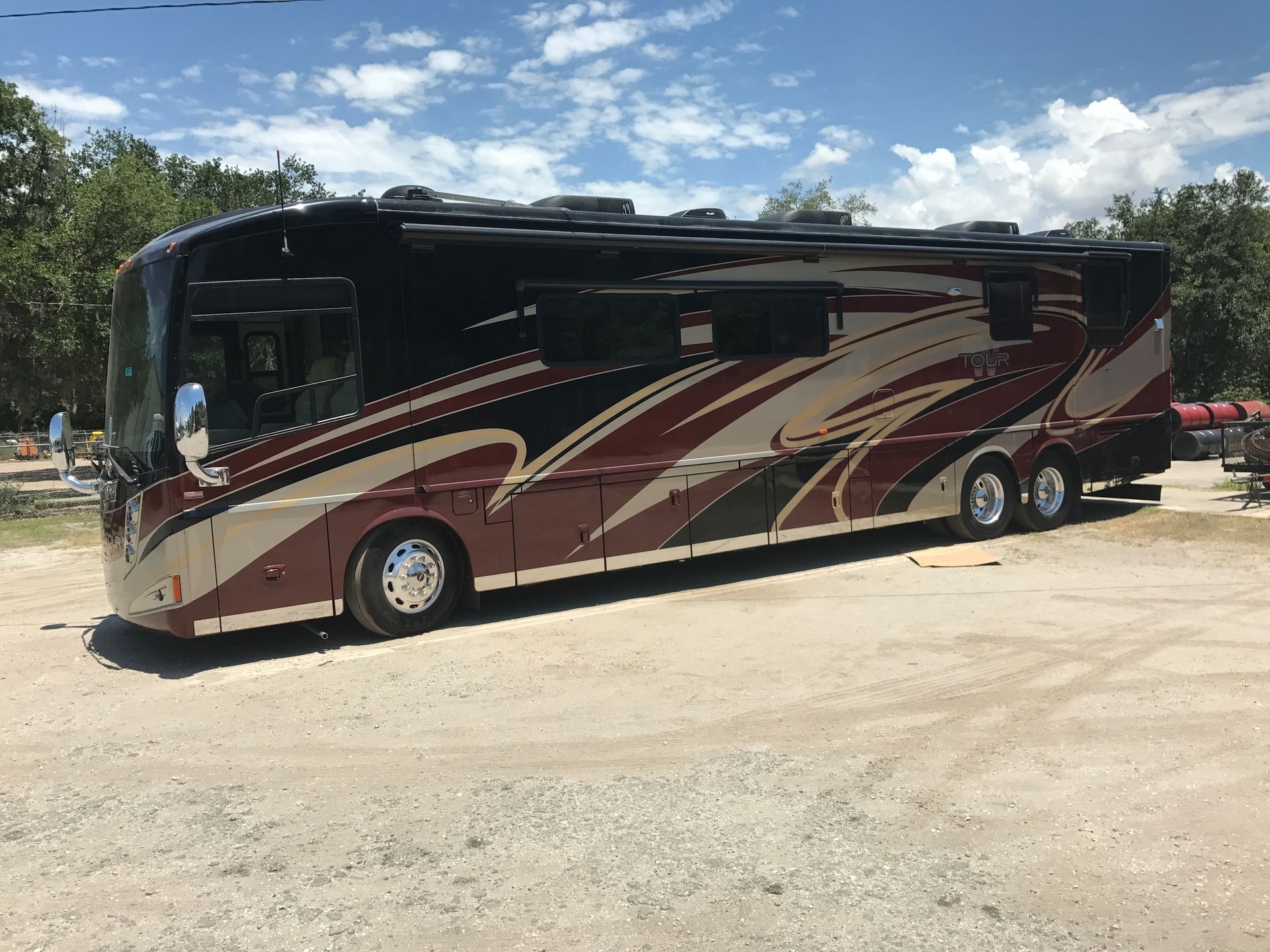 Large maroon and beige motorhome parked on a gravel lot under a cloudy sky