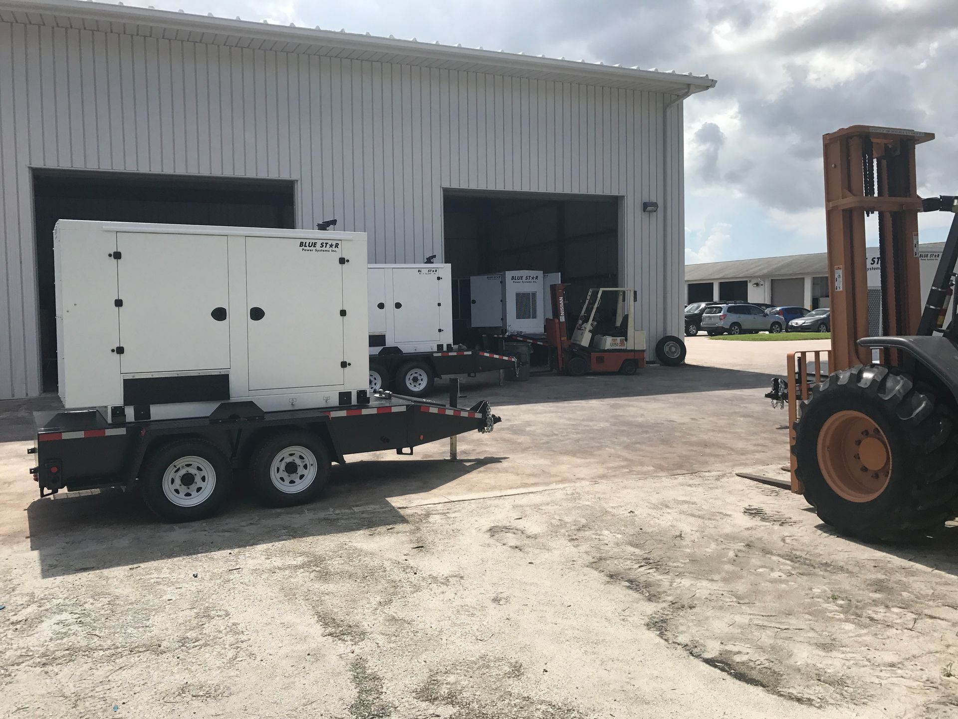 White trailer-mounted generator beside a warehouse, with a forklift on the right.