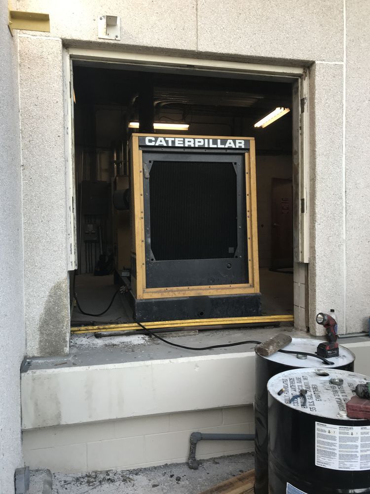 Caterpillar HVAC unit in a wall opening, with a hose and equipment outside.