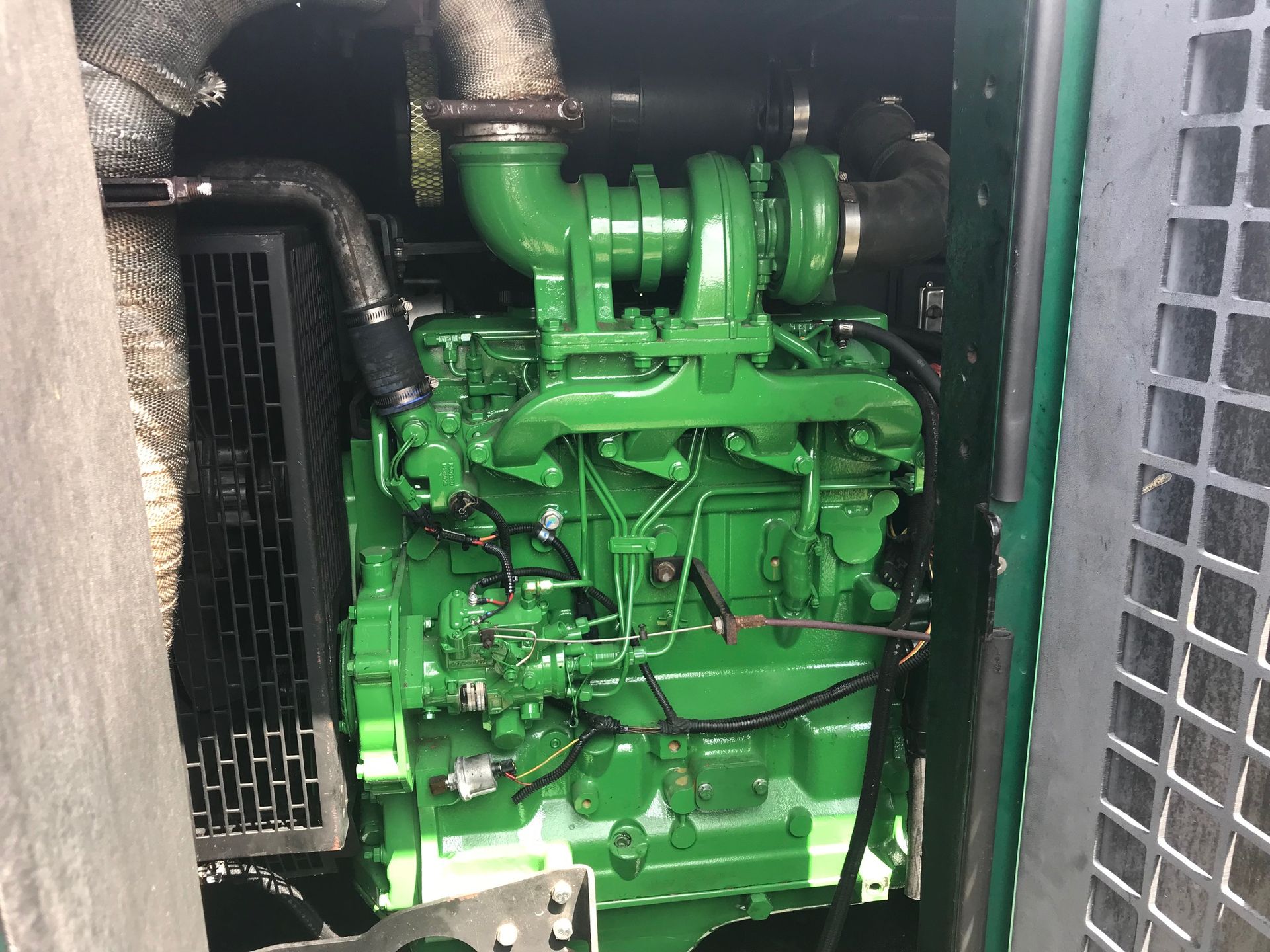 Green industrial engine inside a metal compartment with hoses and vents