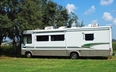 White RV motorhome parked on grass under a blue sky with trees in the background