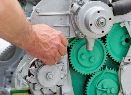 Hand turning a gray gear mechanism with bright green gears inside machinery