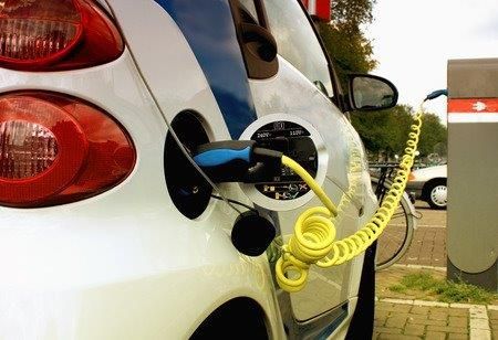 White car charging at an electric station with a yellow coiled cable