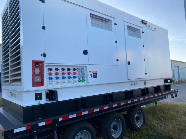 Large white industrial generator mounted on a trailer, parked outdoors on grass.