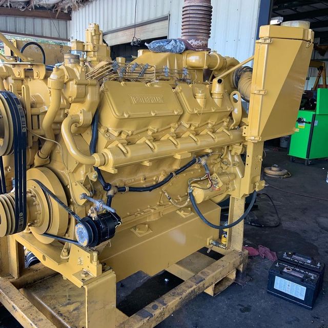Large yellow industrial engine on a pallet in a workshop, with hoses and wiring attached.