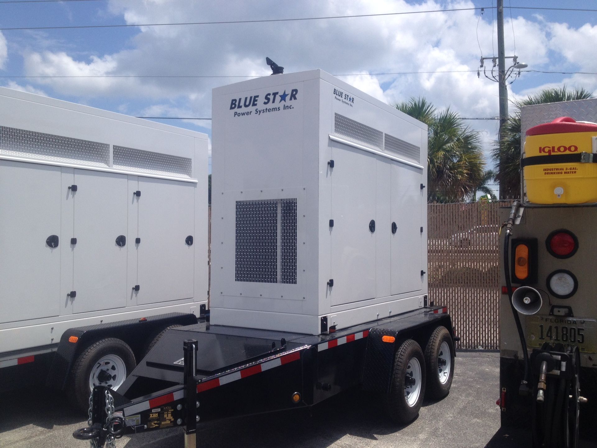 White generator units on black trailers in a parking lot under a cloudy sky
