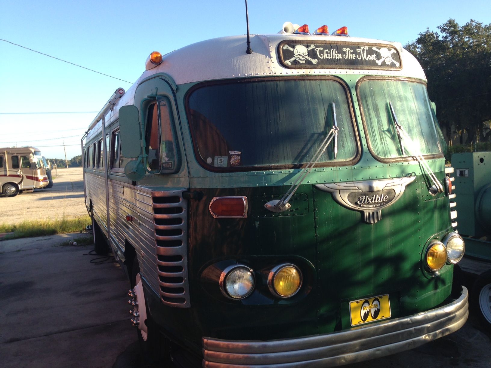 Green vintage bus parked outdoors in sunlight with chrome front and roof lights