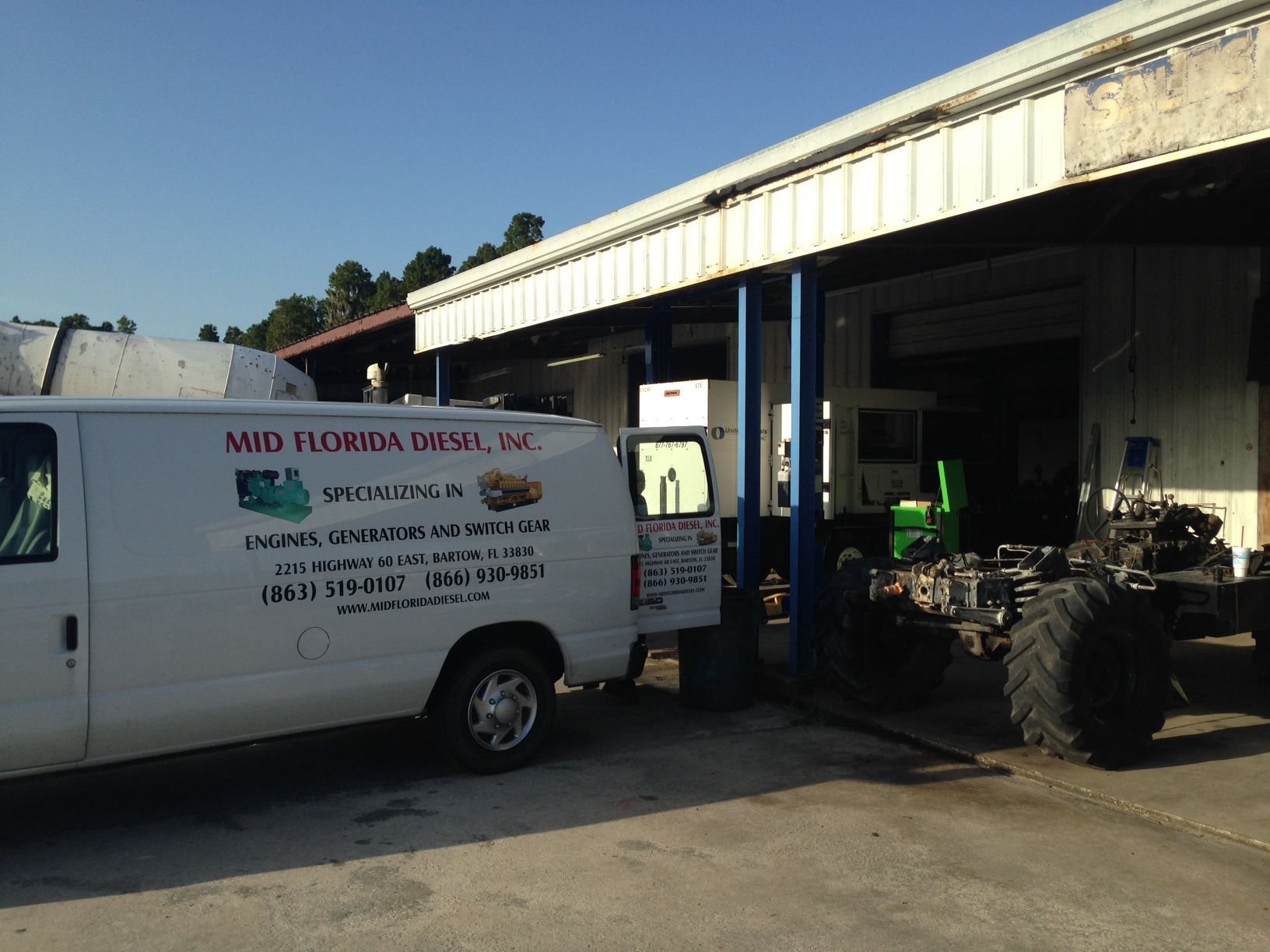 White utility van parked beside a workshop with a tractor inside the open garage.