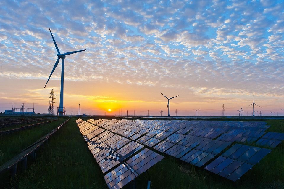 Solar panels and wind turbines at sunrise in a renewable energy field.