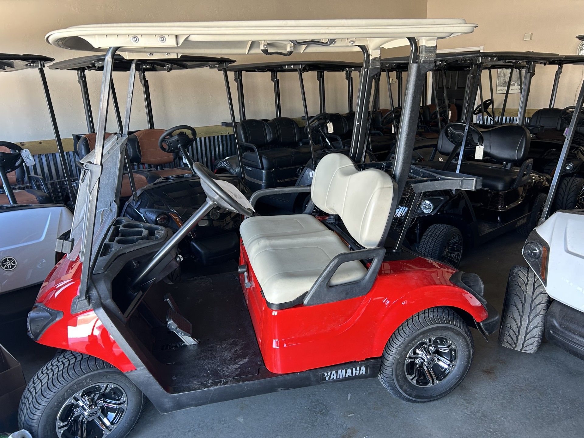 A red golf cart is parked in a garage next to other golf carts.