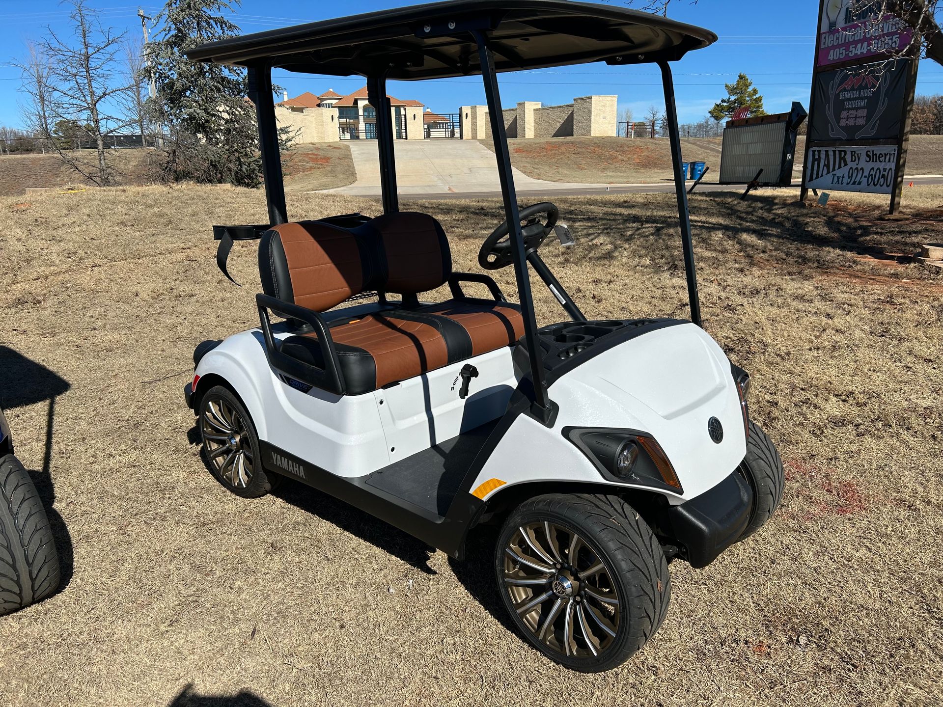 A white golf cart with brown seats is parked in a dirt field