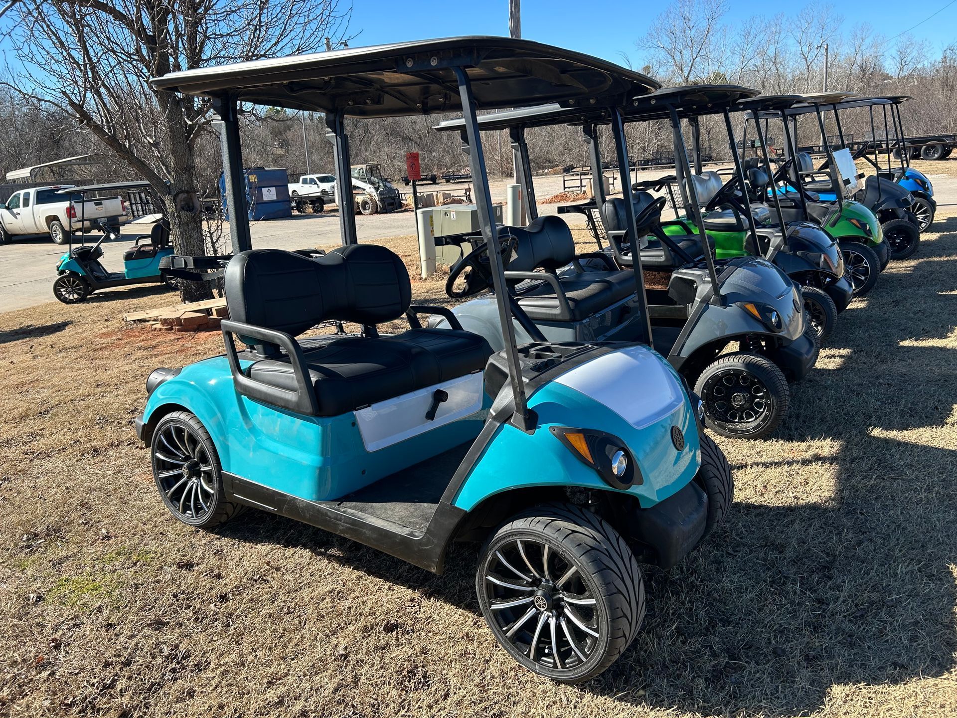 A row of golf carts are parked in a gravel lot