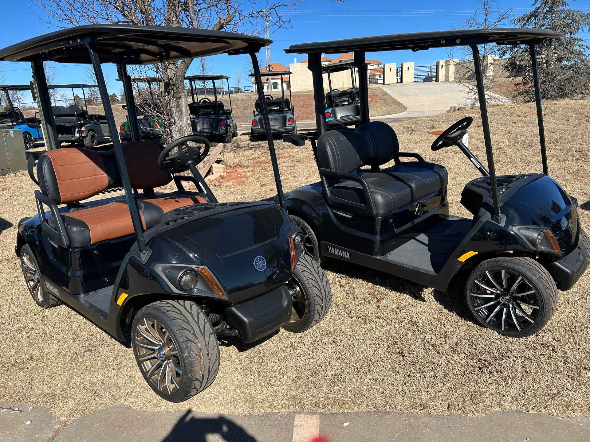 Two black golf carts are parked next to each other in a grassy field