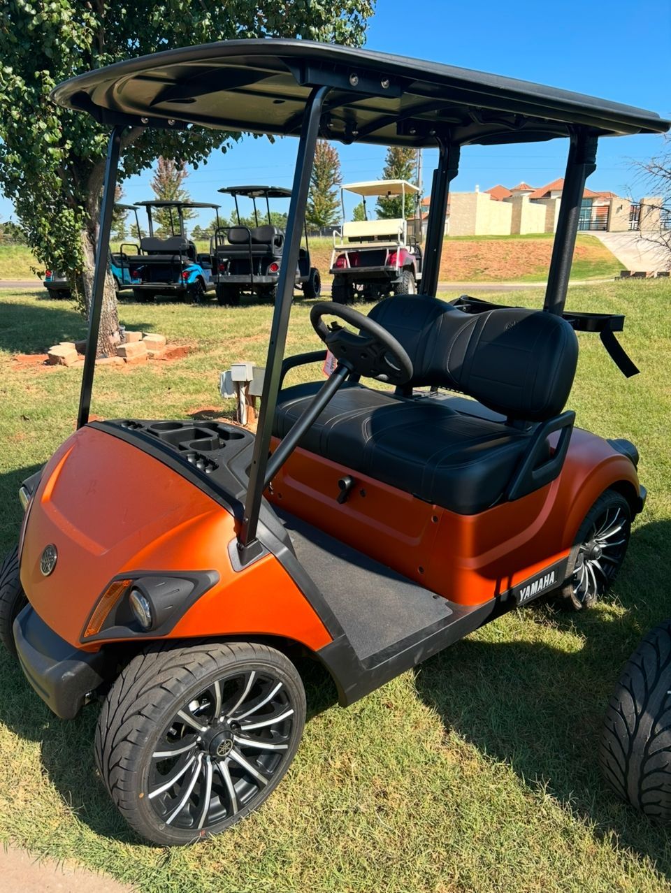 An orange golf cart is parked in a grassy field