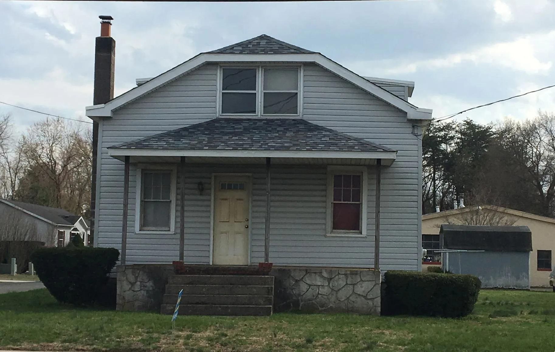 Small light blue house with a covered porch and front steps, on a green lawn.