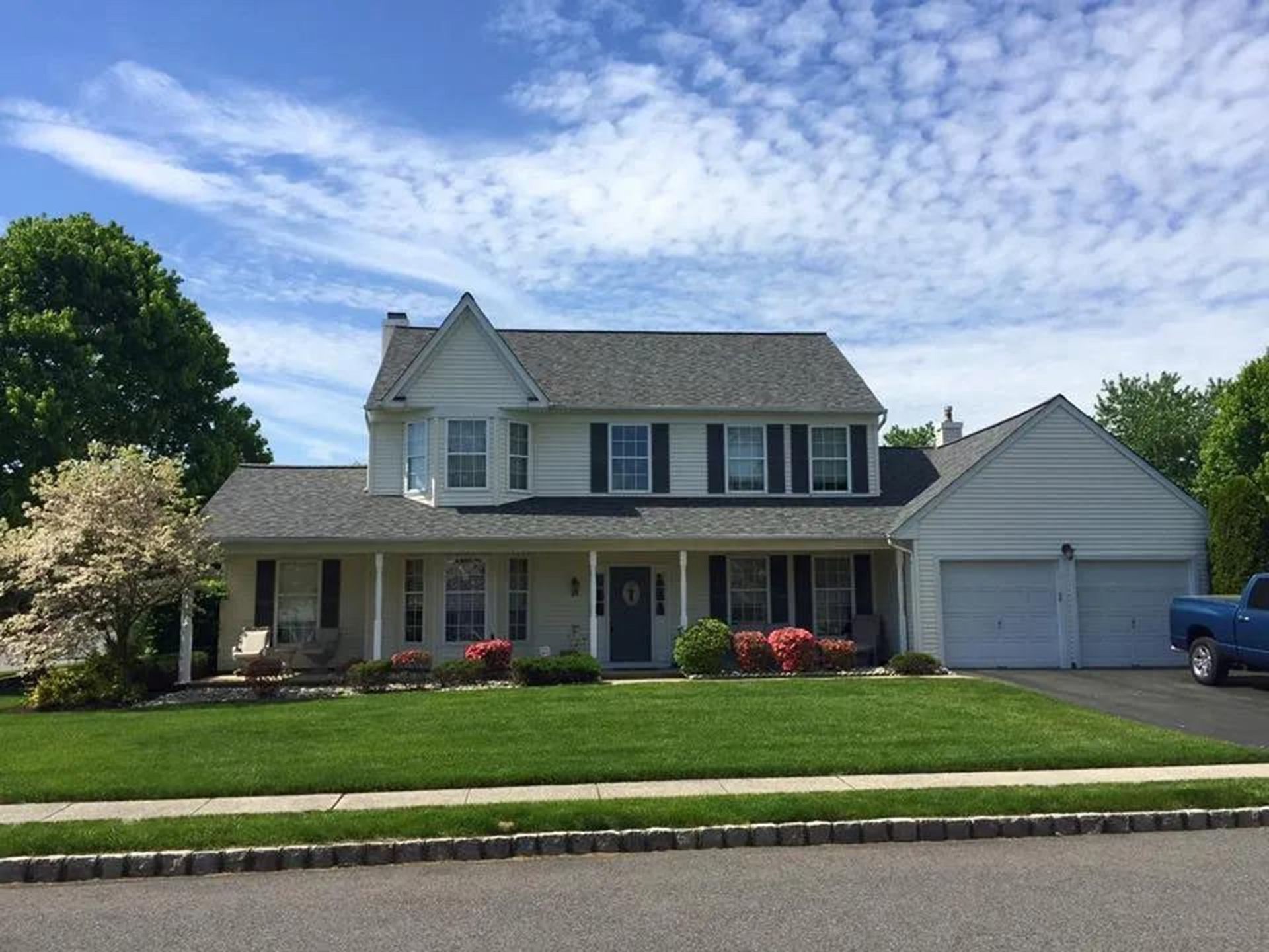 Two-story beige house with black shutters, green lawn, two-car garage, and blue truck on a sunny day.