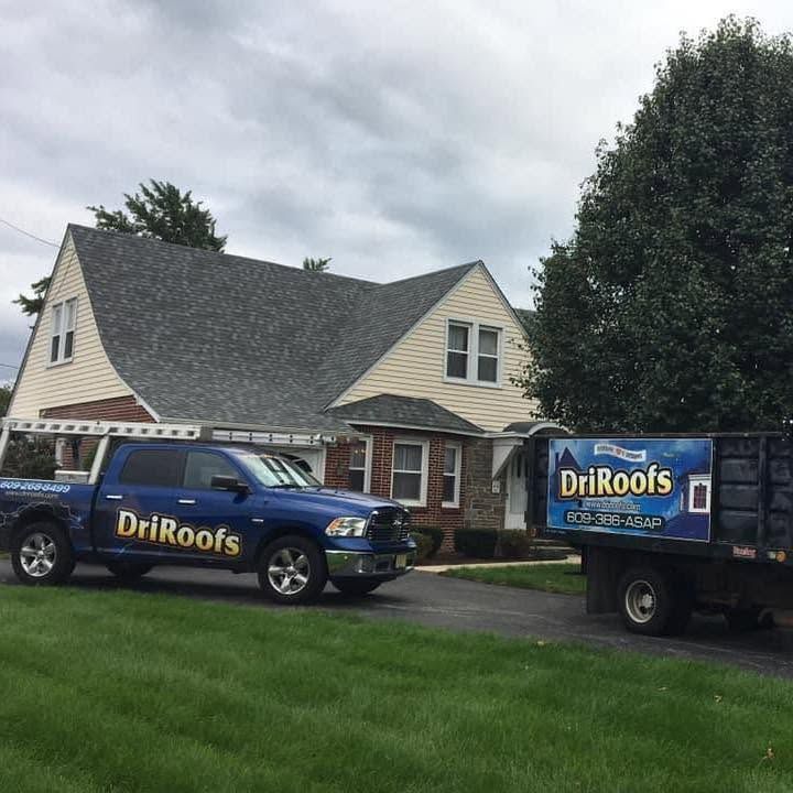 DriRoofs truck and trailer parked outside a house on a cloudy day