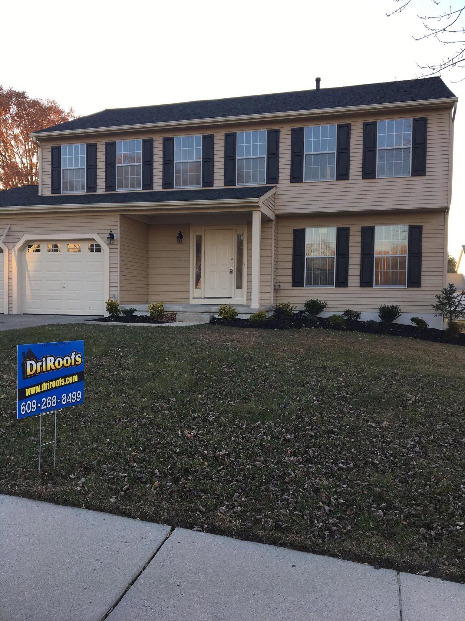 Two-story beige house with blue shutters and a front lawn at dusk, with a real estate sign in the yard