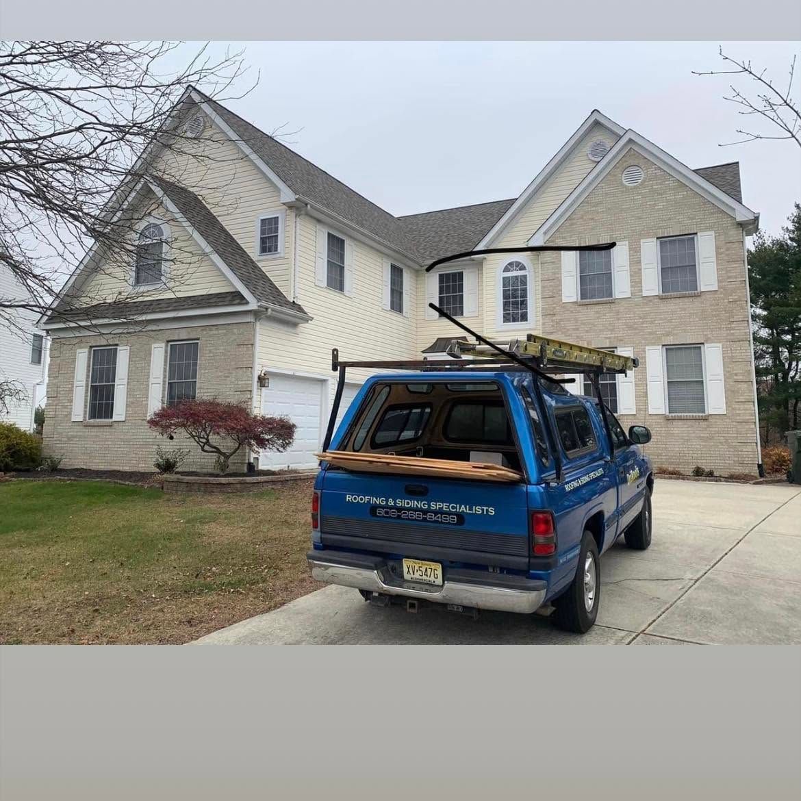 Blue pickup truck parked in front of a beige two-story house with a driveway and lawn