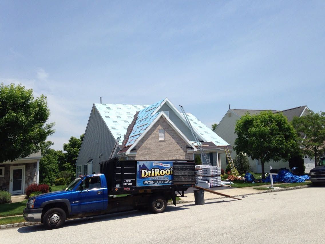Blue truck parked in front of a house under construction with a blue tarp roof and a sign on the truck bed