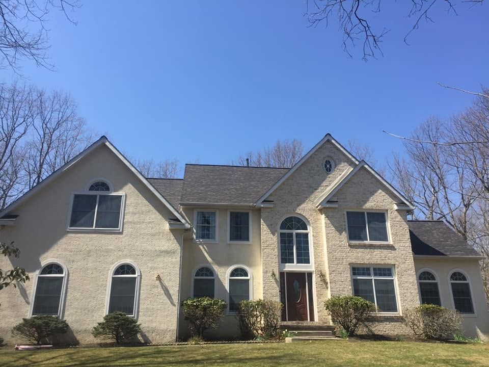 Large beige two-story suburban house with arched windows and a front porch under a clear blue sky