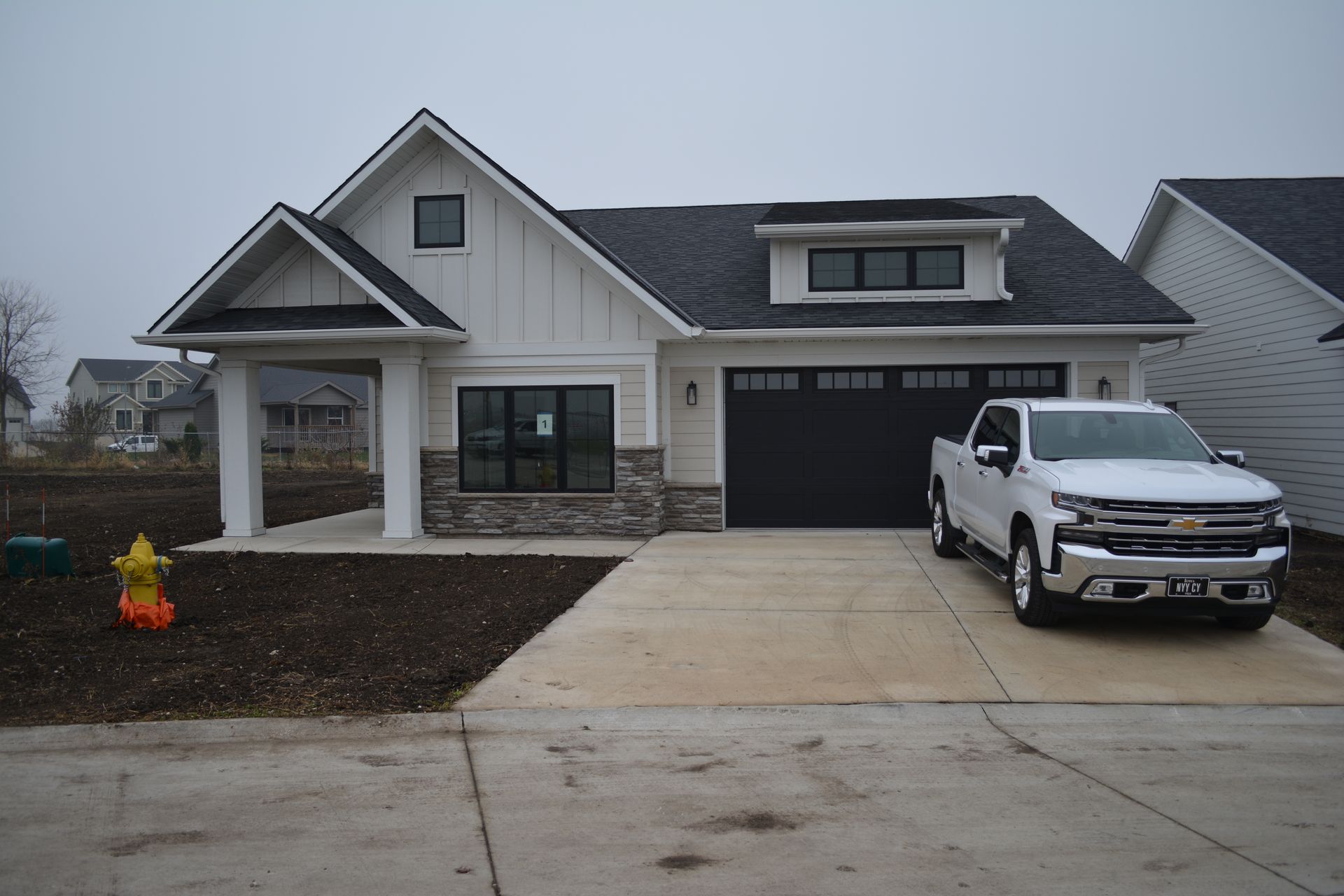 White farmhouse with black garage door and pickup truck parked in driveway. Gray sky.