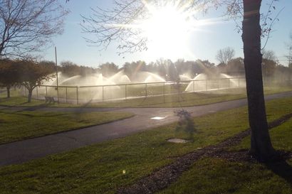 Park sprinklers watering the grass under a bright sun