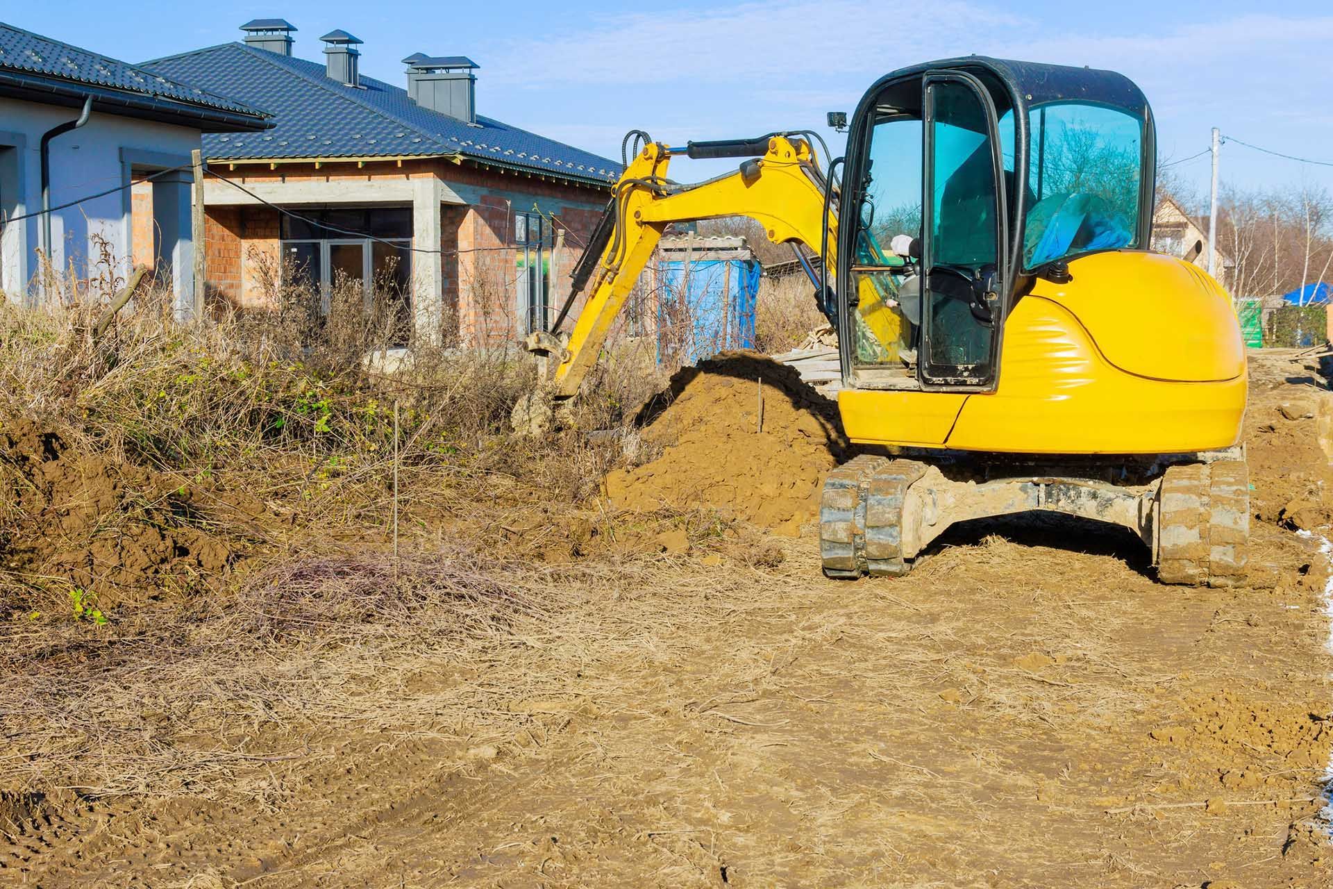 Yellow excavator digging dirt near a house