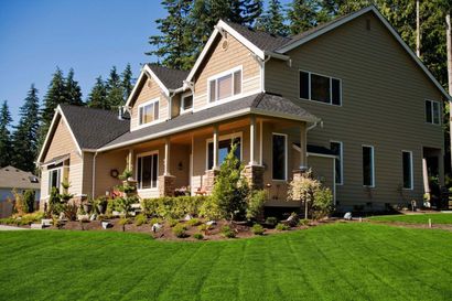 Two-story beige house with a covered porch, surrounded by green grass and trees
