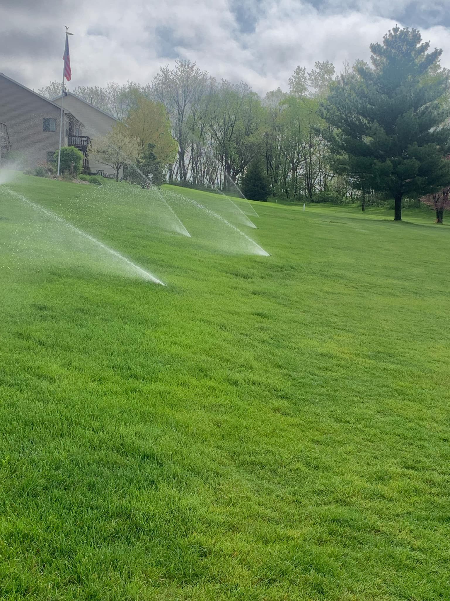 Sprinklers watering a green lawn in front of a building on a cloudy day.