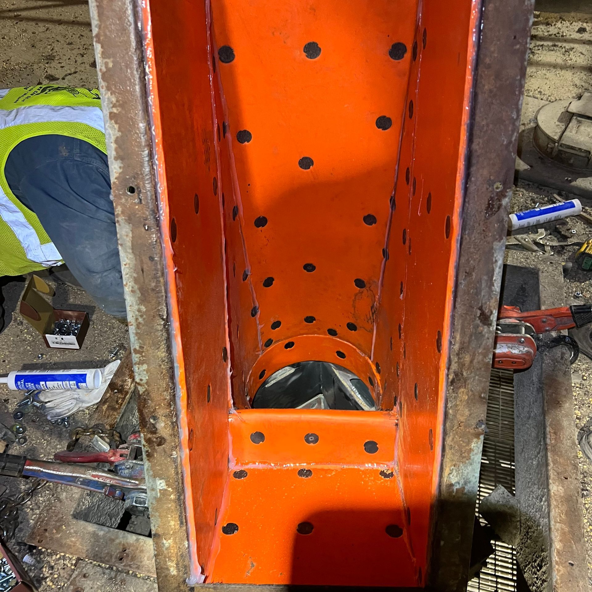 A man in a yellow vest is working on a piece of orange metal