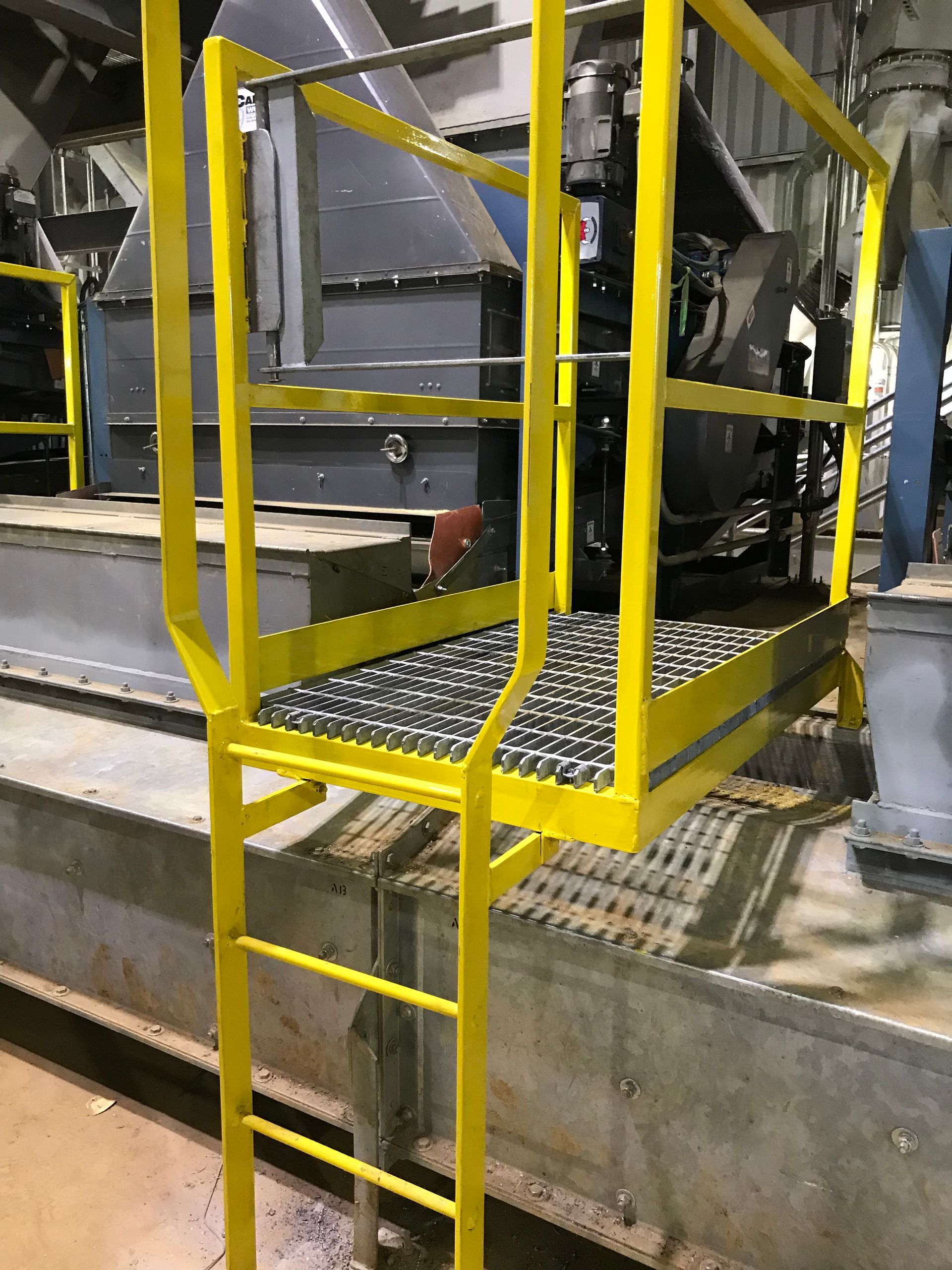 A yellow ladder is attached to a metal platform in a factory