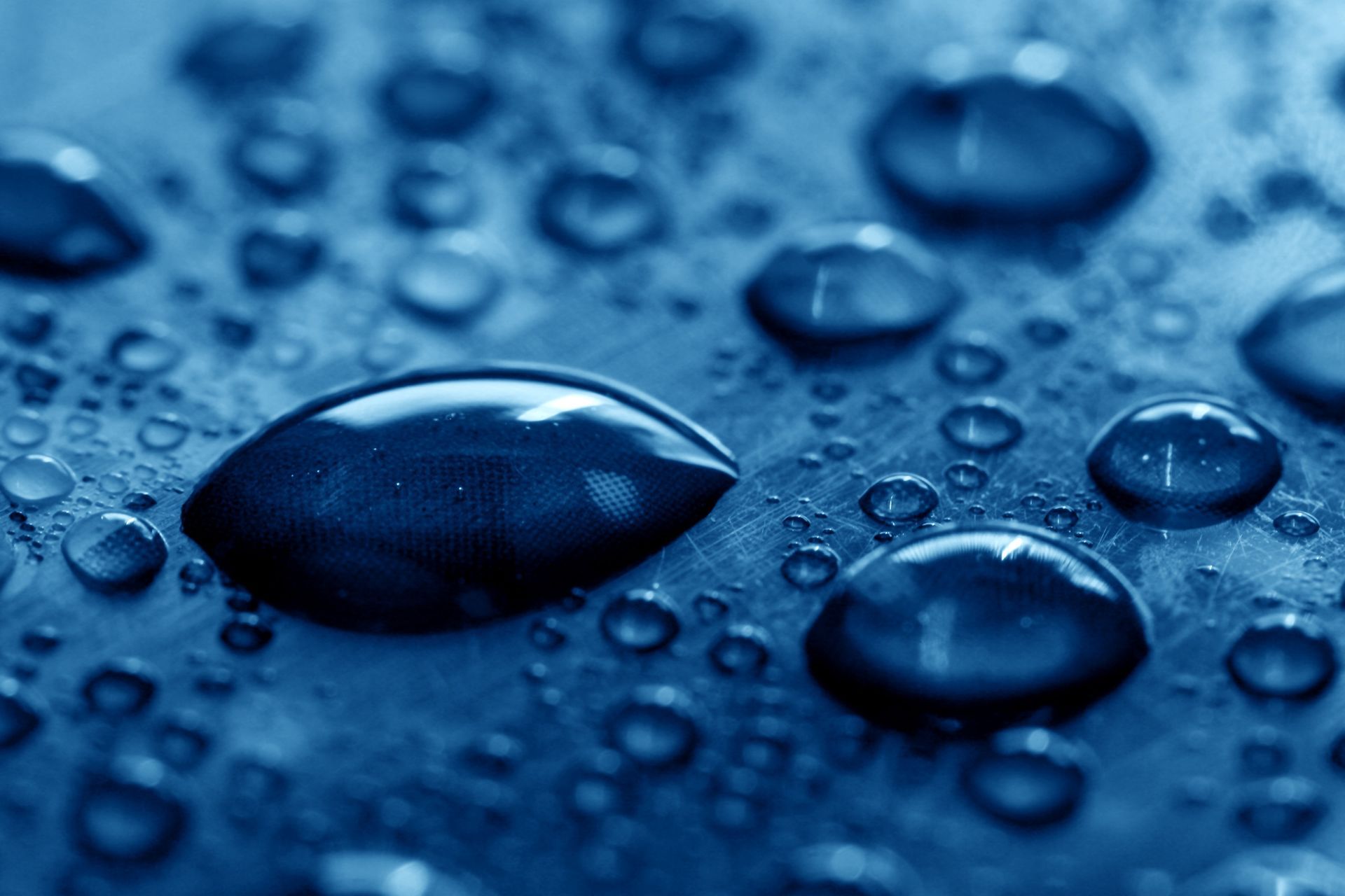 Blue water droplets on a dark blue surface, close-up macro view