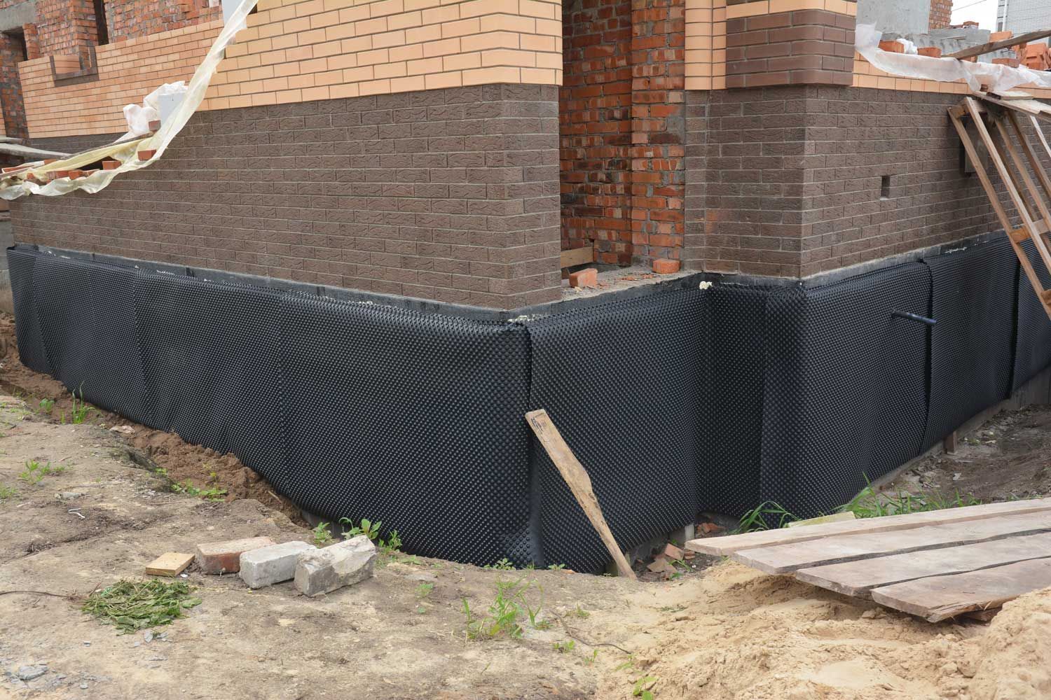 Black foundation waterproofing membrane around a brick house corner during construction