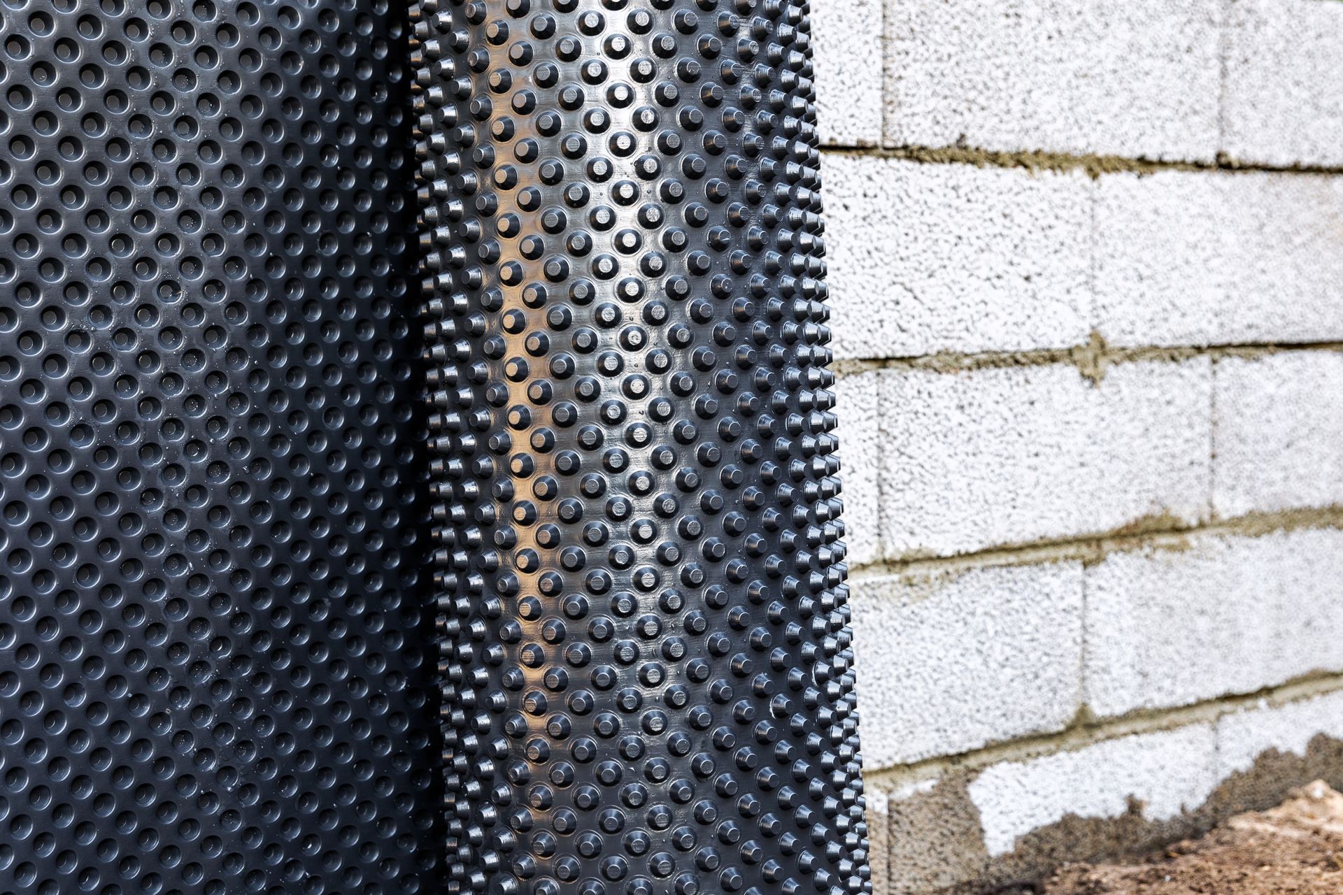 Black dimpled waterproofing membrane against a white cinder block foundation wall outdoors
