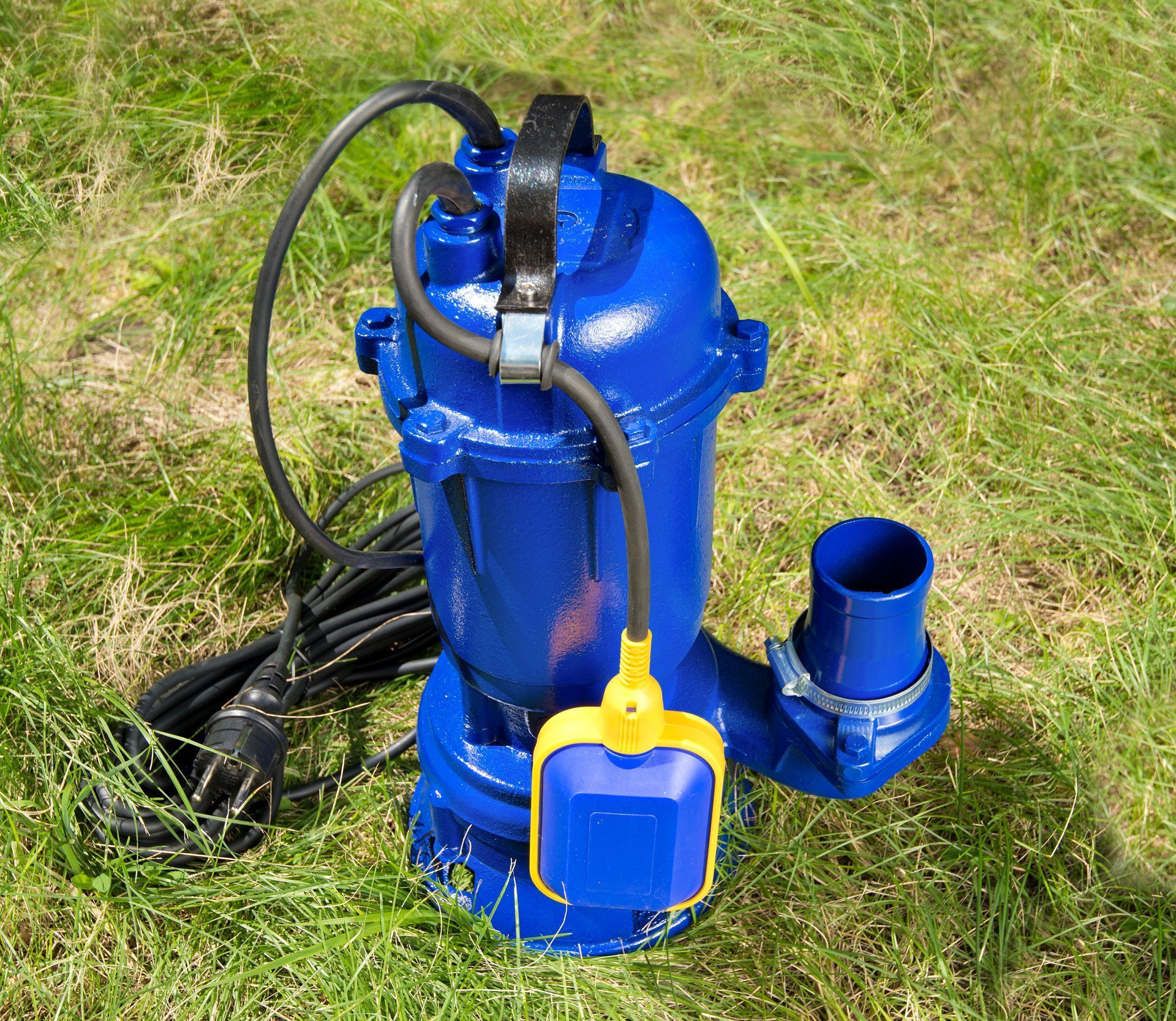 Blue portable pump with hoses and a yellow float switch on grass