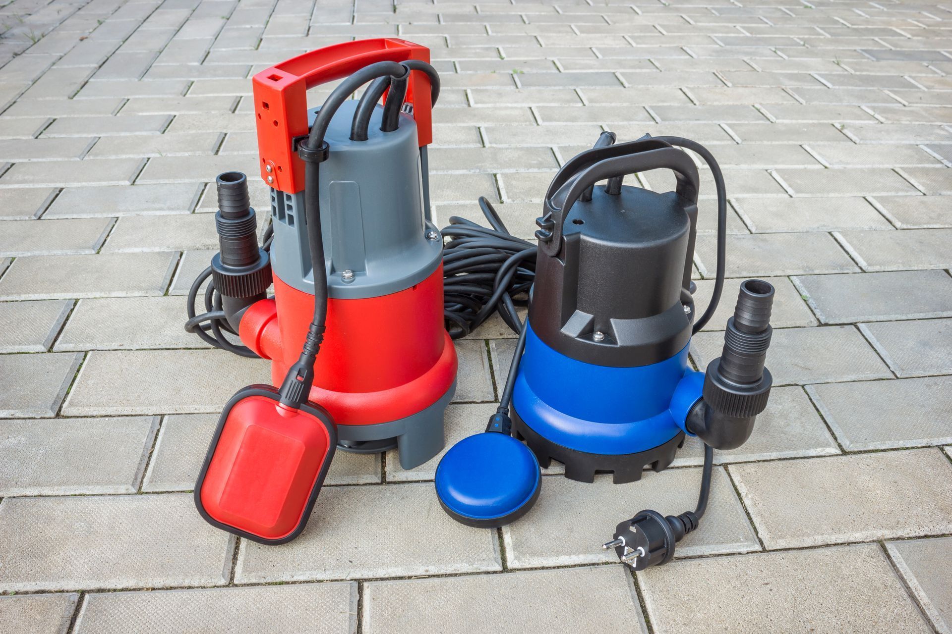 Two portable water pumps, one red and one blue, with cords and hoses on pavement.