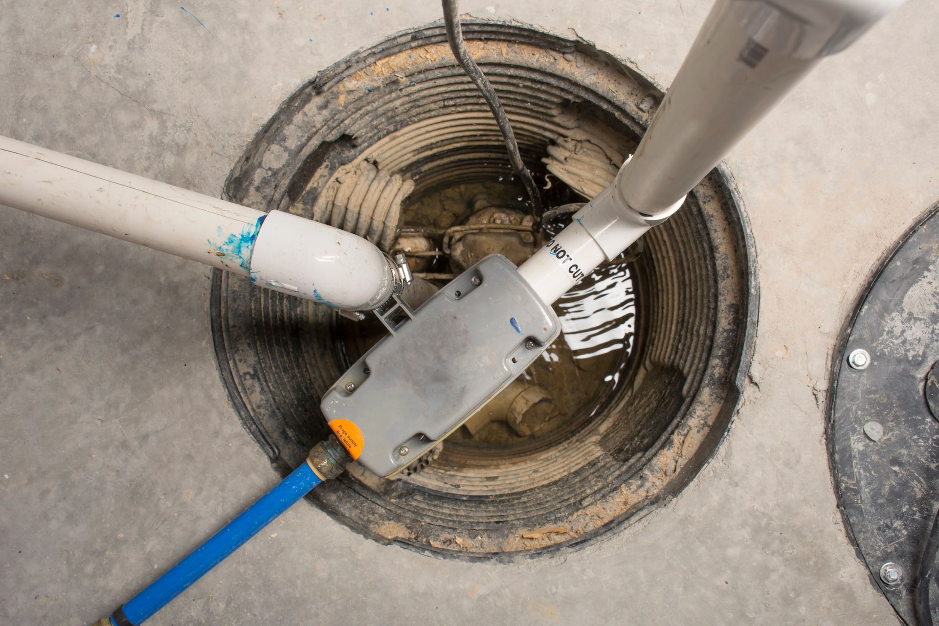 Three pipes and a blue cable entering a concrete manhole with a gray device inside