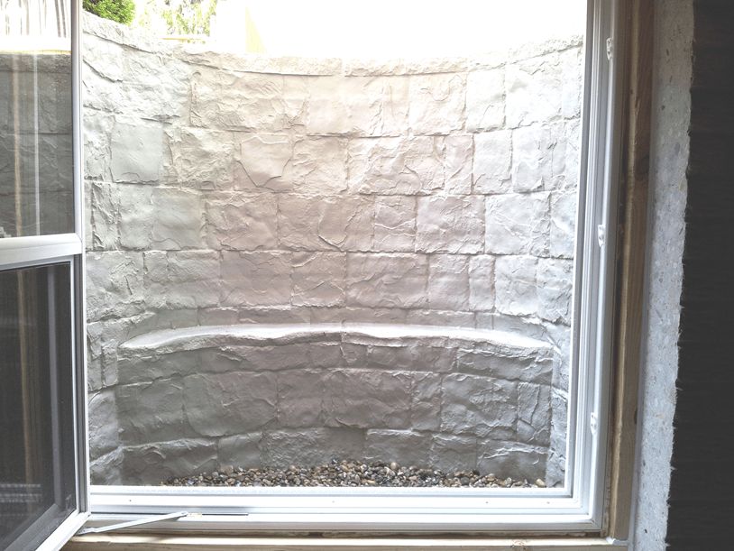Small window looking out onto a white stone wall and ledge.