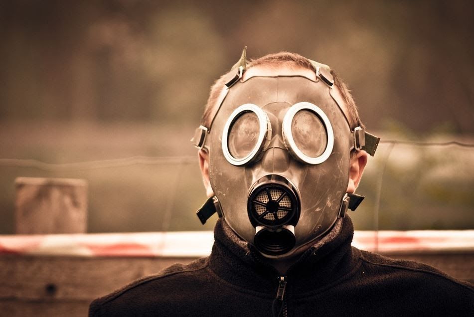 Person wearing a gas mask and goggles against a blurred outdoor background