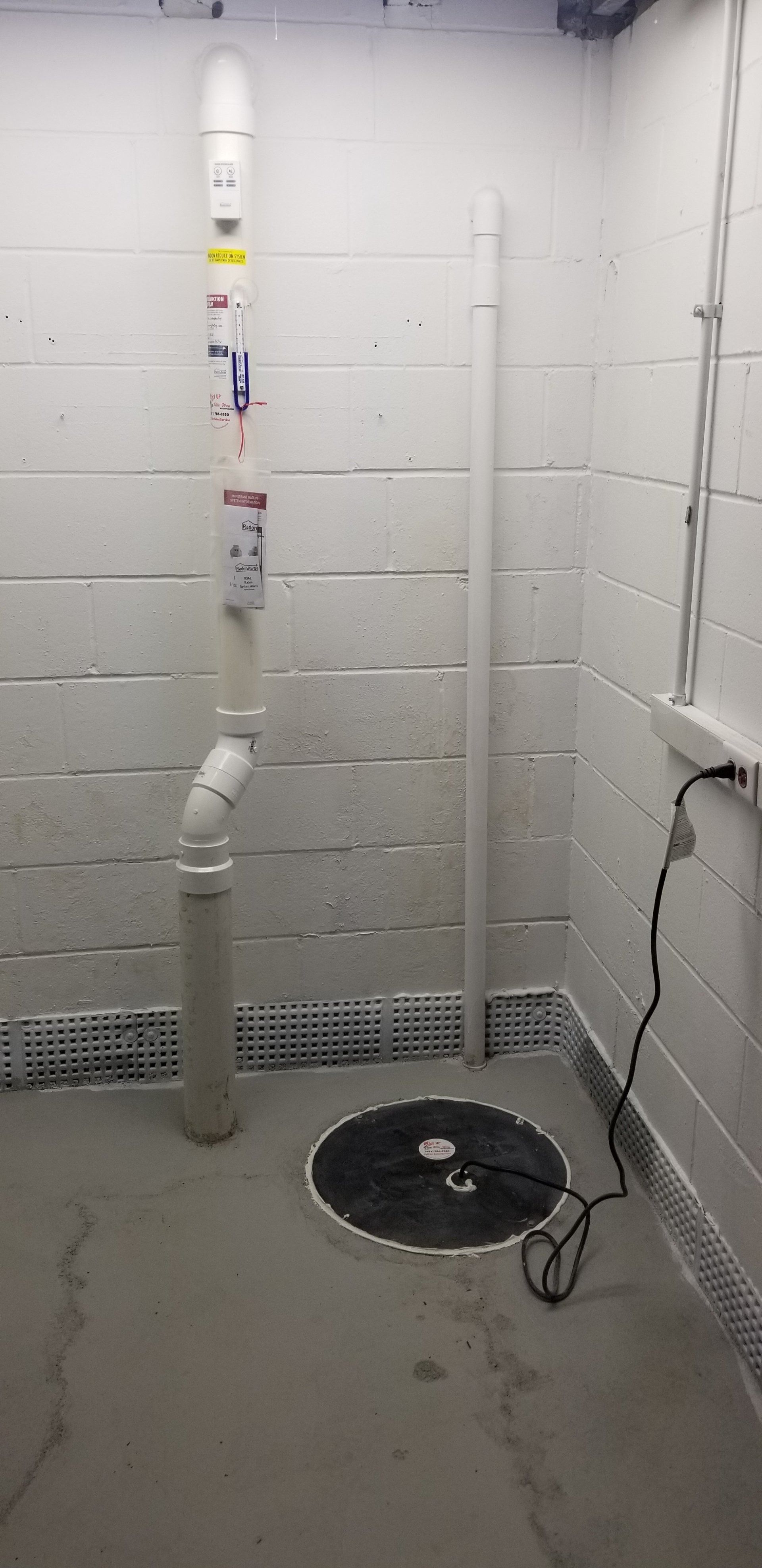 Basement utility room with exposed white pipes, a floor drain, and concrete floor against cinder block walls.